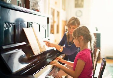 download (4) Mother teaching daughter to play piano. The girl is aged 7. Mother and girls are sitting by the old piano in a sunny room.